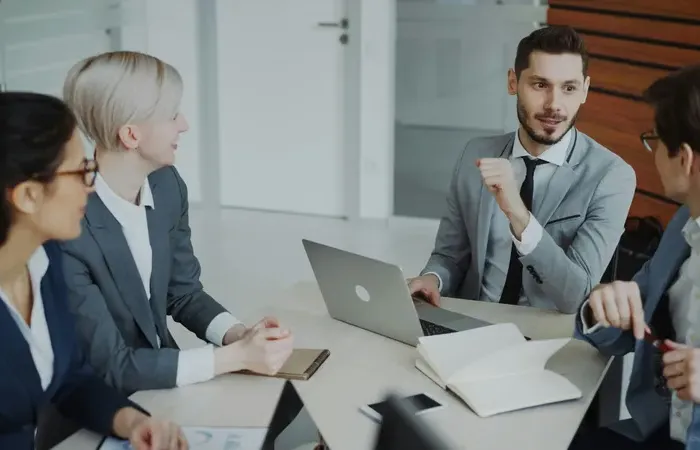Group of business professionals in suits discussing ideas during corporate meeting around office table